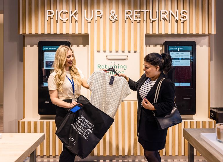 An employee assisting a customer with a clothing return at the 'Pick Up & Returns' station in a Marks & Spencer store.