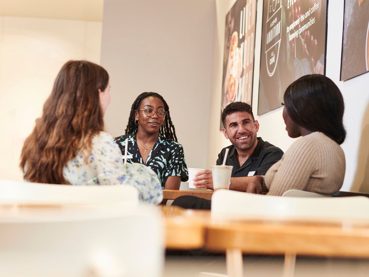 A group of four Marks & Spencer employees sitting together in a café, engaged in conversation while having drinks.