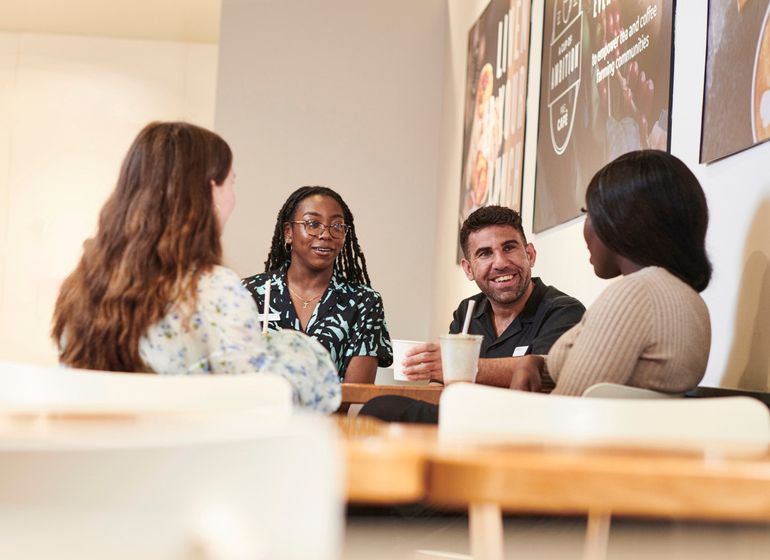 A group of four Marks & Spencer employees sitting together in a café, engaged in conversation while having drinks.