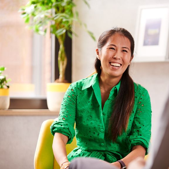 A woman smiling and laughing, sitting down in a bright office setting.