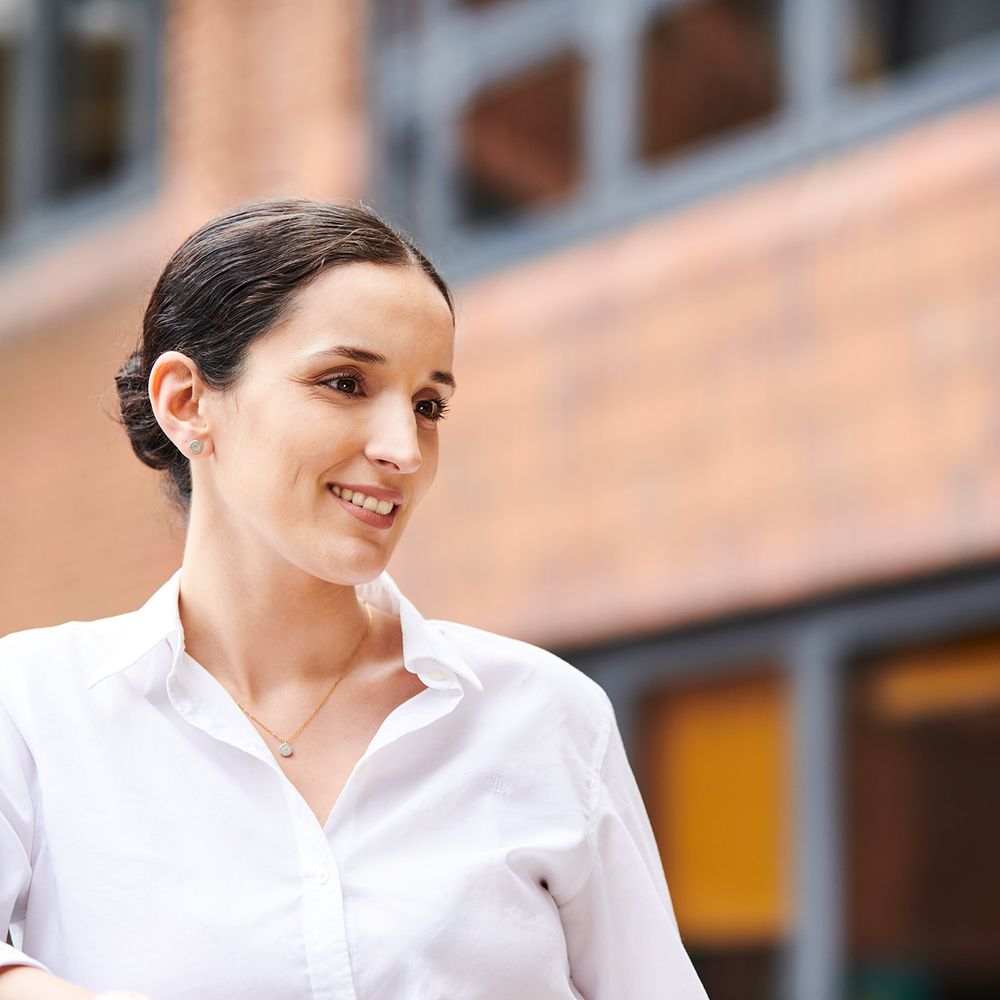 A woman smiling, looking into the distance outside a building.