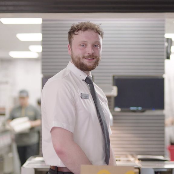 A man with a beard wearing a white shirt and tie stands inside a fast food restaurant.