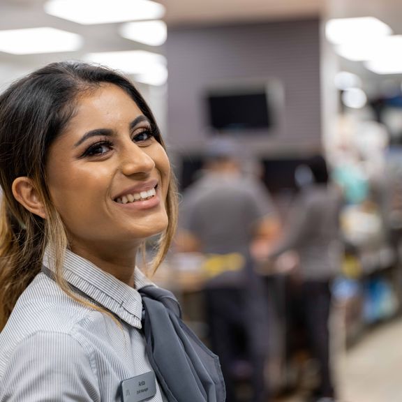An employee smiling in grey uniform in a fast-food kitchen.