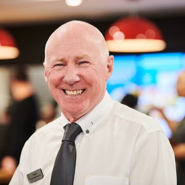 A cheerful man wearing a white shirt and grey tie standing in a fast-food restaurant.