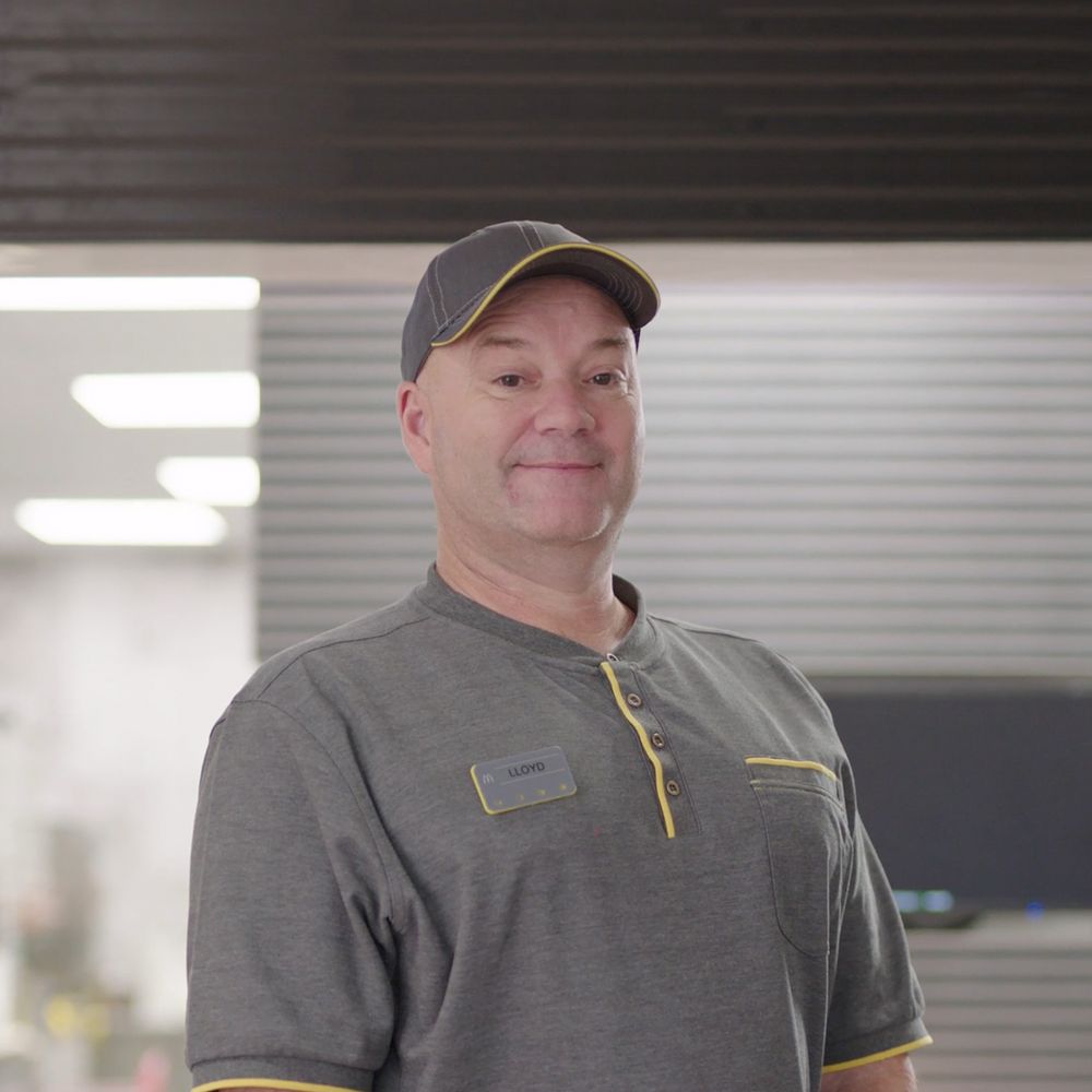 An employee in a grey uniform standing and smiling in a fast-food restaurant.
