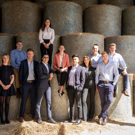 A group of eleven individuals posing in front of hay bales.