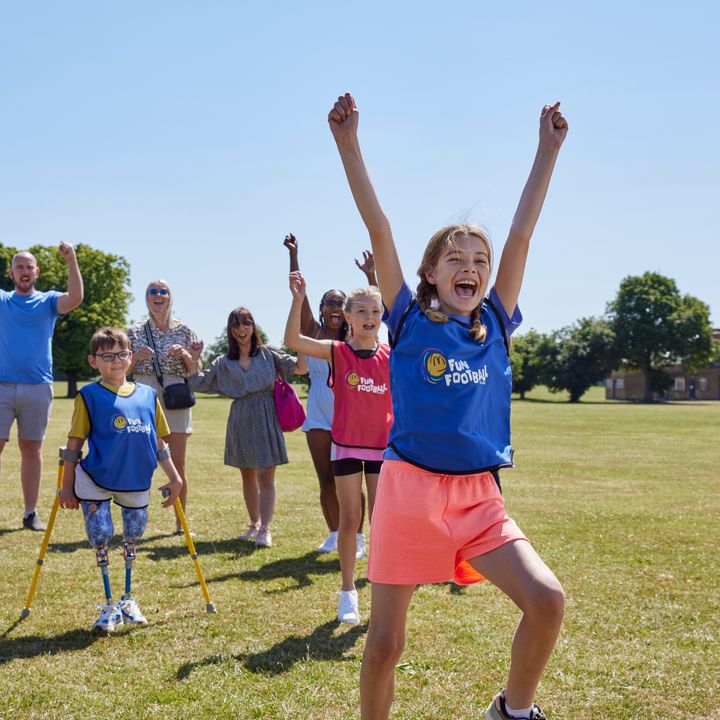 A group of children and parents raising their arms in joy, outside under a clear blue sky.