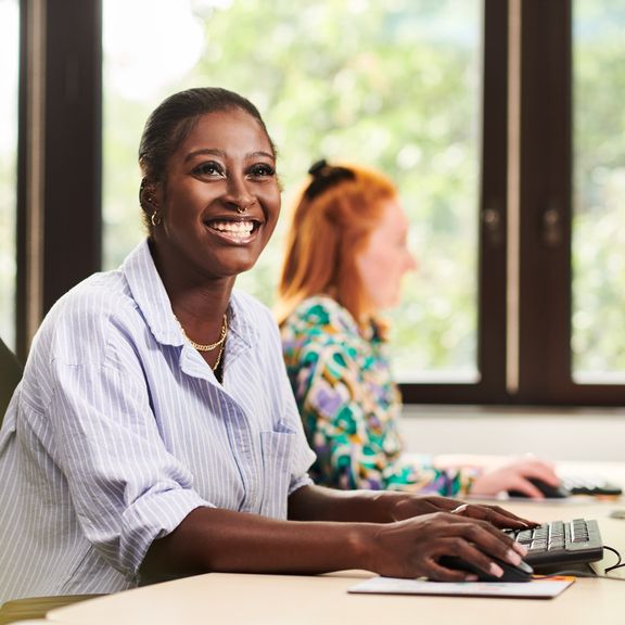 Two cheerful individuals sitting side by side at a desk, both using their keyboards, in an office setting.