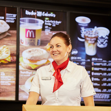 An employee in a white shirt with a red tie, standing behind a counter, ready to assist customers with a friendly smile.