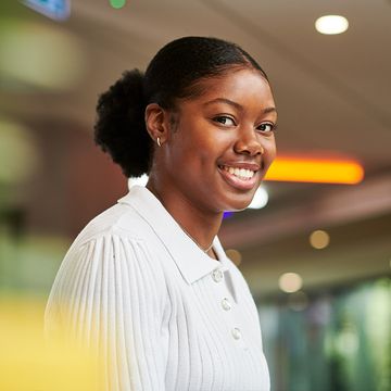 A woman wearing a white shirt, smiling in a bright office.