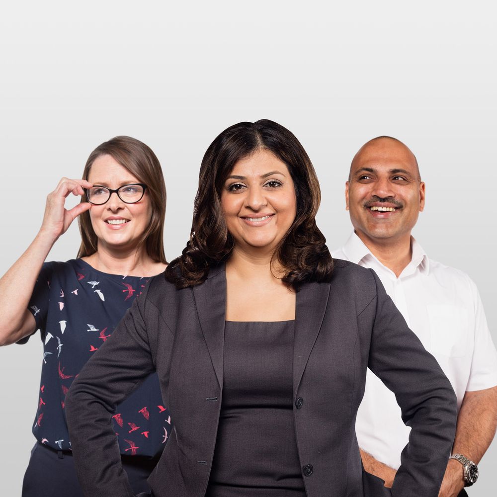 Three smiling people: a woman with glasses, a woman in a dark suit, and a man in a white shirt, against a light grey background.