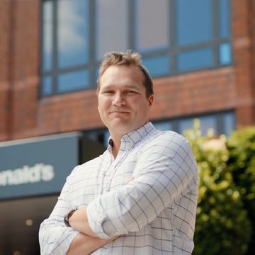 A man smiling, with arms crossed, standing outside a building.