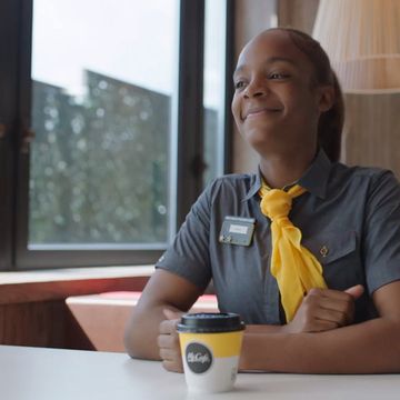 Employee in uniform with a yellow scarf sitting at a table with a coffee cup.