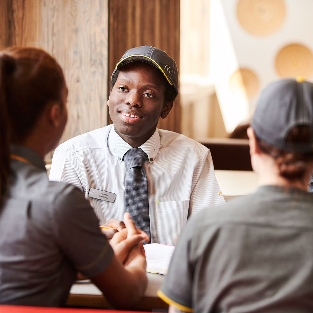 Three employees in grey uniform, sitting at a table chatting in a fast-food restaurant.