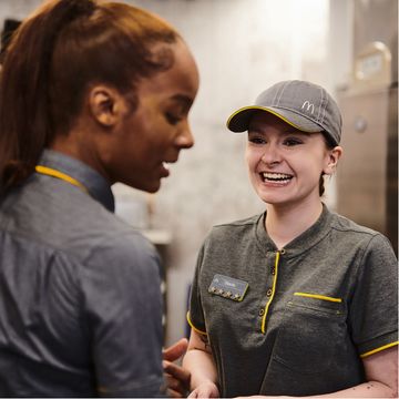 Two employees in grey uniforms, one has a hat and is smiling.