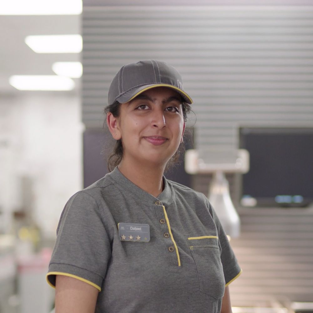 Employee in gray uniform standing in a fast-food restaurant.