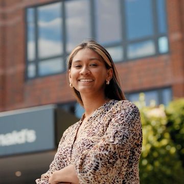 A woman smiling, with arms crossed, standing outside a building.