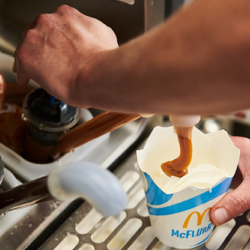 A hand pouring chocolate sauce into a cup filled with ice cream.