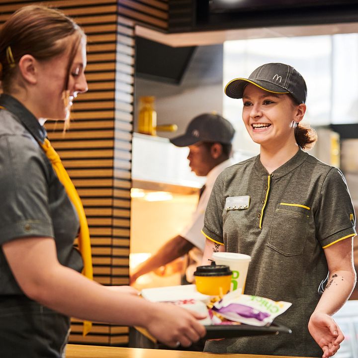 Two employees in a fast-food restaurant, one handing over a tray of food.