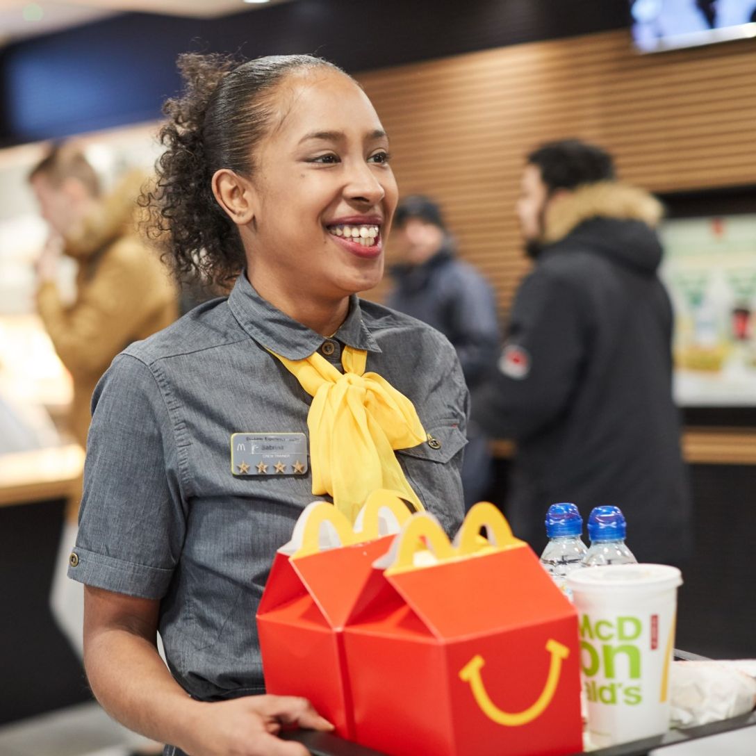 An employee at a fast-food restaurant holding a tray of food and a refreshing drink, ready to serve to customers.