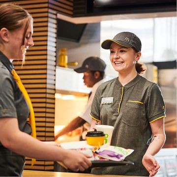 Two employees in a fast-food restaurant, one handing over a tray of food.