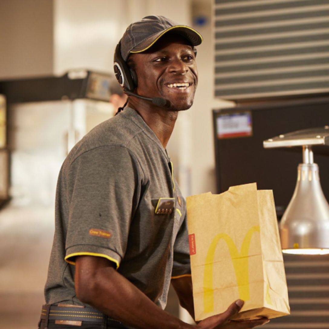 A fast-food employee in a grey uniform, preparing a takeaway bag of food.