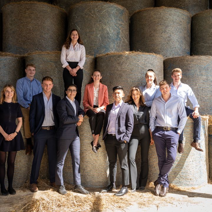 A group of eleven individuals posing in front of hay bales.