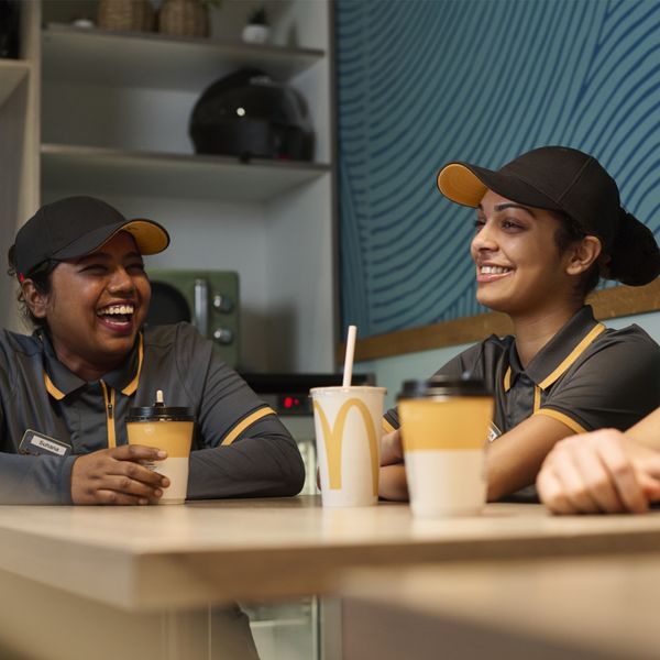 Three employees in a fast-food restaurant smiling, wearing gray polo shirts and black caps.