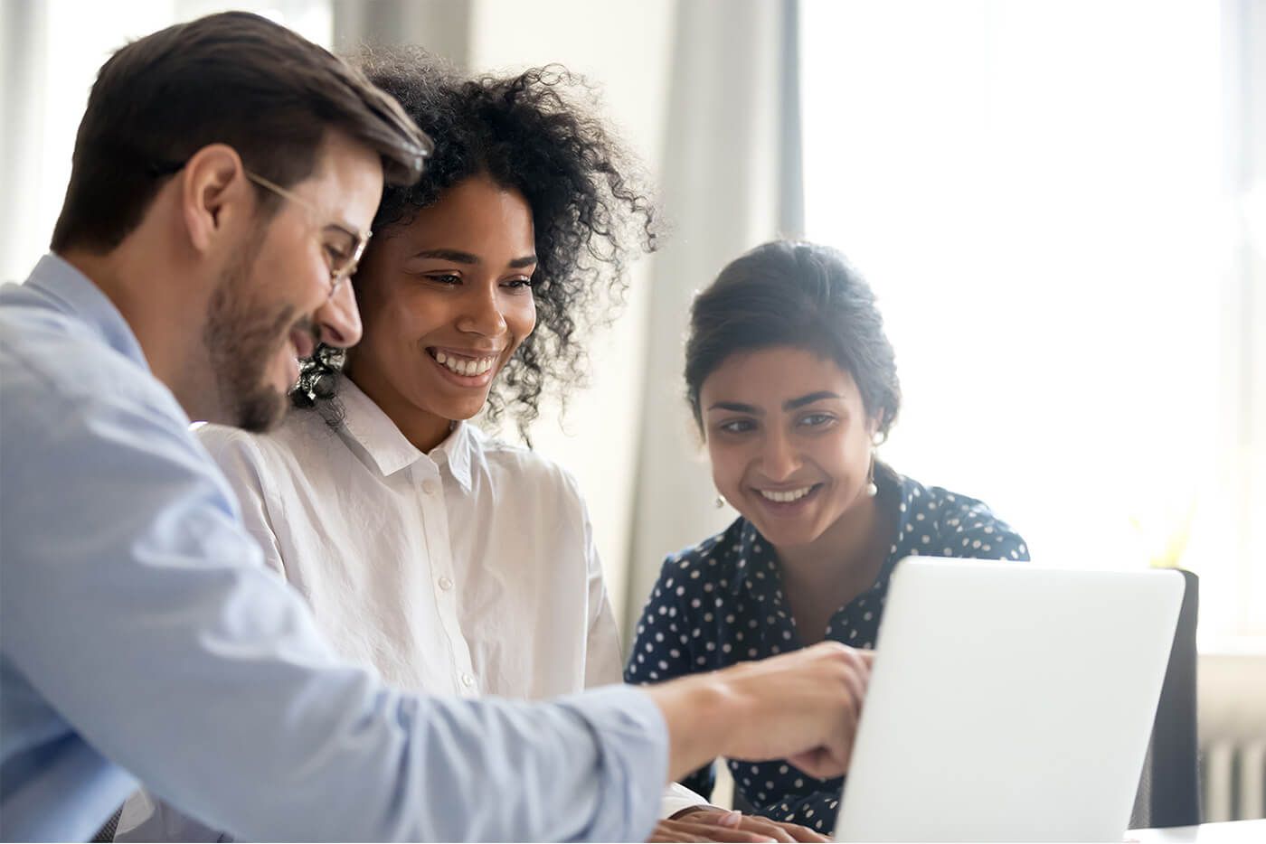 Life at MSCI_Internal Mobility. Three colleagues gathered around a laptop, smiling and engaged in a discussion in a bright office setting.
